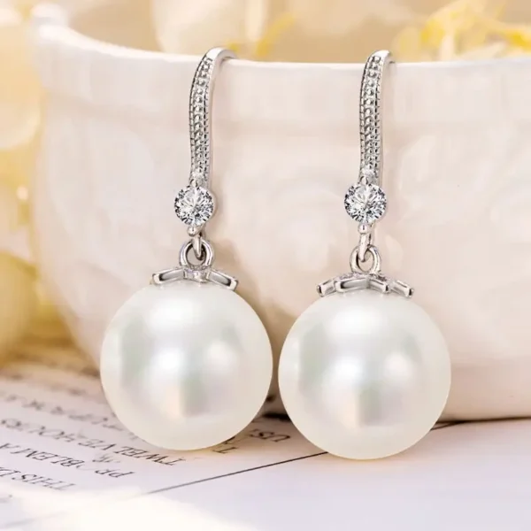 A pair of white pearl drop earrings with a silver-toned metal frame and small diamond accents.