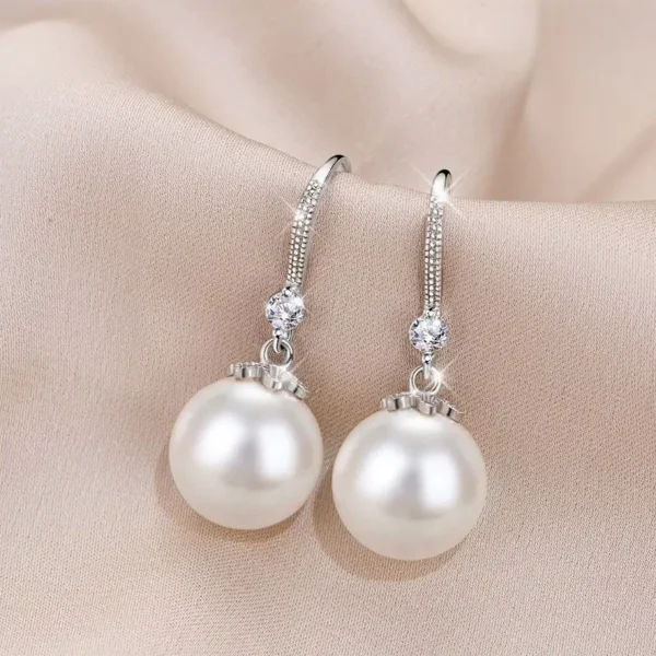 A pair of white pearl drop earrings with a silver-toned metal frame and small diamond accents.